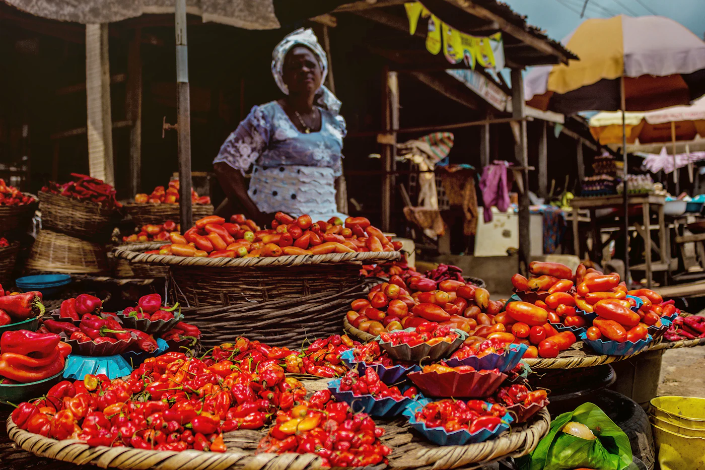 Vendeuse au marché derrière ses paniers de tomates et de piments